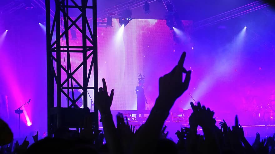 Sebuah konser musik, banyak tangan yang terangkat, seorang penyanyi berdiri di tengah panggung